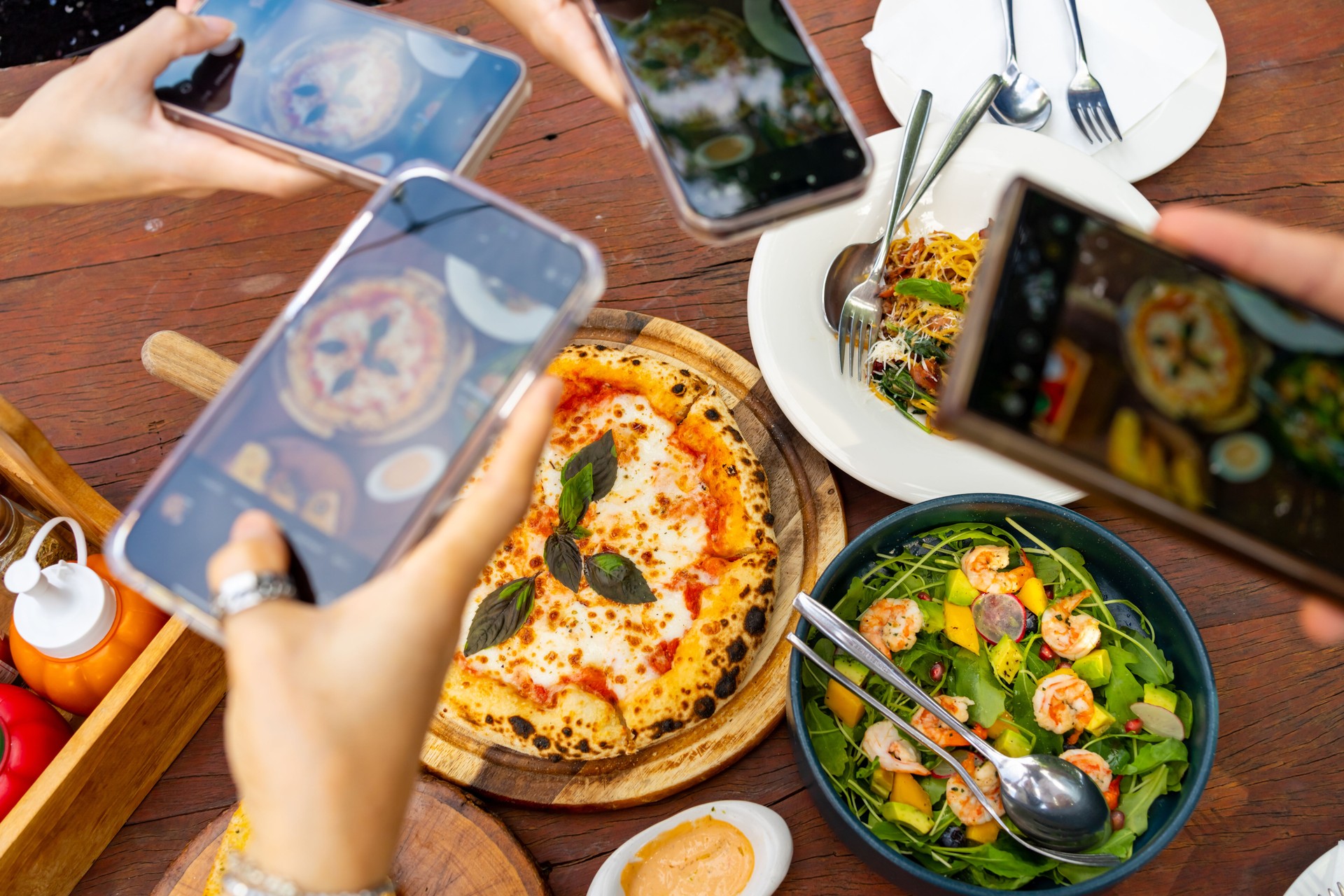 Group of Asian people using smartphone taking picture of food on dining table.